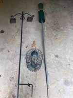 Photo showing all three bird feeders on a concrete floor: black wrought iron double feeder stand with two mesh baskets, a green cylindrical hanging feeder with metal pole, and a round cage-style feeder with metal top.