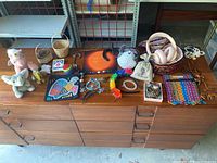 Full layout of all items on wooden dresser showing colorful beaded jewelry, patches, noise canceling headset in Vera Bradley case, small baskets, animal figurines, and necklaces.
