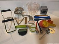 Photo of all 19 cooking utensils including masher, measuring cup, peelers, scissors, spatulas, measuring cups, and juicer arranged on counter.
