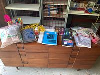 Photo of entire lot spread out on dresser including sketchbooks, markers, paint set, yarn, fabrics, glue, and flowers.