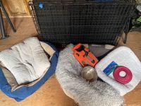 Photo showing assorted dog beds, a dog harness, a dog bowl, a dog toy, and the wire pet crate.