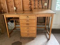 Front view of wooden drafting desk with central column of six drawers, wood finish, and left side adjustable surface flat.