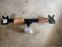 Full view of black metal Class III trailer hitch receiver with mounting brackets, partially wrapped in brown paper, laying on concrete floor.