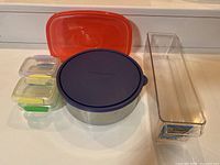 Various food storage containers displayed on a white surface including plastic containers and a U-Konserve stainless steel container with lid