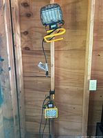 Photo showing smaller job site light mounted on adjustable wooden stand with yellow extension cord wrapped around it and attached power cord