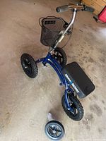 Blue KneeRover knee scooter angled view showing padded knee rest, basket, and extra small wheel on the ground beside it.
