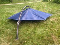Full view of large navy blue outdoor cantilever umbrella lying on grass. Curved metal arm and crank handle visible.