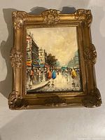 Full view of Paris scene oil painting in ornate gilded frame placed on a flat surface.