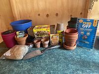 Photo showing various terra cotta and plastic pots, seed starter packets, soil amendment bag, metal hand trowel, and a garden pest repellant spray box.