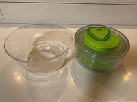 Photo displays a green salad spinner with lid and inner basket next to a clear mixing bowl on a countertop.