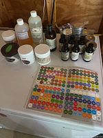 Wide view of assorted organic oils and butters with bottles, tins, and sheet of sticker labels on table.