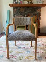 Front view of chair showing wooden armrests and geometric patterned seat and backrest upholstery against a carpeted floor.