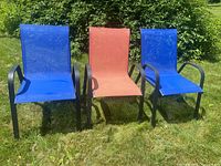 Front view of three stackable outdoor chairs, two with blue mesh seats and one with red, black aluminum frames, placed on grass.