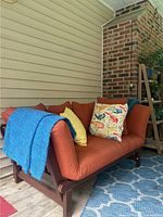 Wide-angle photos showing the full settee from front and side, highlighting cushions, pillows, and throws with close-up of wooden frame detail.