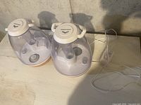 Two Sharper Image ultrasonic humidifiers placed side by side on a light surface with cords visible, showing top and side views with control knobs and mist spouts visible.