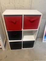 White shelving unit showing 6 cubbies with 4 fabric storage baskets (2 red on top row, 2 black on bottom rows) and two empty cubbies