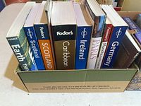 Photo of eight travel and geography books arranged vertically in a box with visible titles and brands.