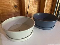 Two round plant pots with matching saucers in light beige and gray colors on a wooden surface