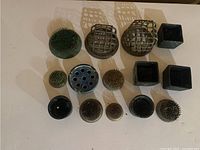 Top-down view of all 14 metal flower frogs showing different shapes and sizes including round and square with grids and spikes.