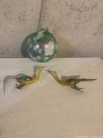 Photo showing the round green and white spotted glass Christmas ornament with two yellow bird-shaped glass figurines featuring colorful wing accents and feather tails.