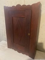 Front view of vintage wooden medicine cabinet with scalloped edges and closed door showing wood grain and keyhole lock.
