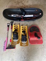 Photo of black sled, yellow Fimbultvetr snow shoes, red Zipfly sled and three ice scrapers on concrete floor.