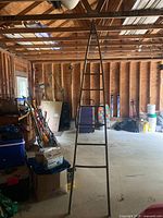 Full vertical view of tall wooden ladder standing upright in the garage among other stored items.