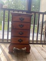 Full view of small wooden dresser showing four drawers and bracket feet, placed on wood floor with outdoor background