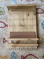 Front view of the wooden wall organizer showing wires, shelf with cork backing, and hooks.