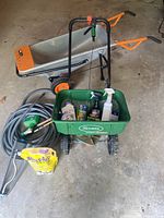 Full view of wheelbarrow, spreader, coiled hose with spray nozzle, and assorted garden products inside the spreader hopper. Items show signs of use but no visible damage.
