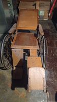 Front angled view showing wooden seat, armrests, metal-spoked wheels, and footrest.