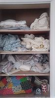 Folded assorted bedding in neutral colors on shelves including white, cream, blue, and patterned fabrics