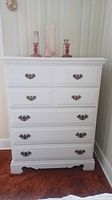 Front view of white wooden dresser with five drawers and vintage metal handles.