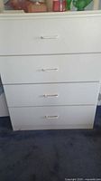 Front view of white four drawer dresser showing all four drawers closed, with simple white handles and a clean white finish.