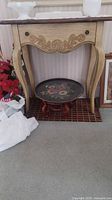 Wooden entry table with curved legs and carved floral apron. Light wood finish. Tray on floor underneath table.