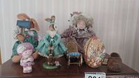 Lot displayed on wooden surface against striped wallpaper, showing five figurines including bunnies, doll and Easter egg