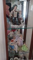 Full display case view of all figurines on glass shelves, showing arrangement and various figurines including mothers with children and musical girl