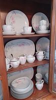 Full view of china in wooden cabinet, showing arrangement of plates, platters, cups, cream and sugar bowl with floral patterns