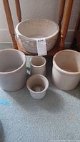 Five ceramic flower pots shown, three main pots visible, ceramic, off white and beige tones, one large with decorative embossed swirl pattern