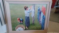 Full view of framed oil painting showing a woman hanging clothes and a child playing by laundry basket.