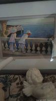 Photo of framed art print of two children leaning on a balustrade by water, along with porcelain cherub figurine in front
