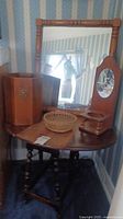 Photo showing entire drop leaf table with multiple items on top including mirror, basket, candle holder, and waste basket beside it.