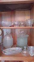 Shelf with an assortment of clear glass and crystal items including bowls, plates, a candy dish, and a gravy boat.