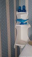 White corner shelf mounted on wall holding two blue glass birds on top shelf and a blue glass dolphin on middle shelf.