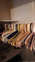 Photo showing many assorted plastic hangers in peach, white, yellow, pink colors and some metal hangers towards the back, hanging on a closet rod.