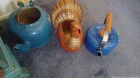 Three items shown: two tea kettles (one blue metal with wooden handle, one blue ceramic), and a brown ceramic turkey figurine