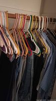 Men's clothing on hangers in closet, including pants and shirts