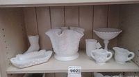 Shelf with assorted milk glass items: large ruffled floral vase, pedestal candy dish, small rectangular dish, and 3 small creamers.