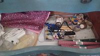 Wide view of sewing lot including fabric, hot glue gun, thread spools, buttons, and ribbons inside a container drawer
