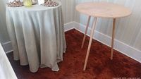 Two round tables shown, one covered with cloth and the other wooden visible. Contents on top of covered table excluded.